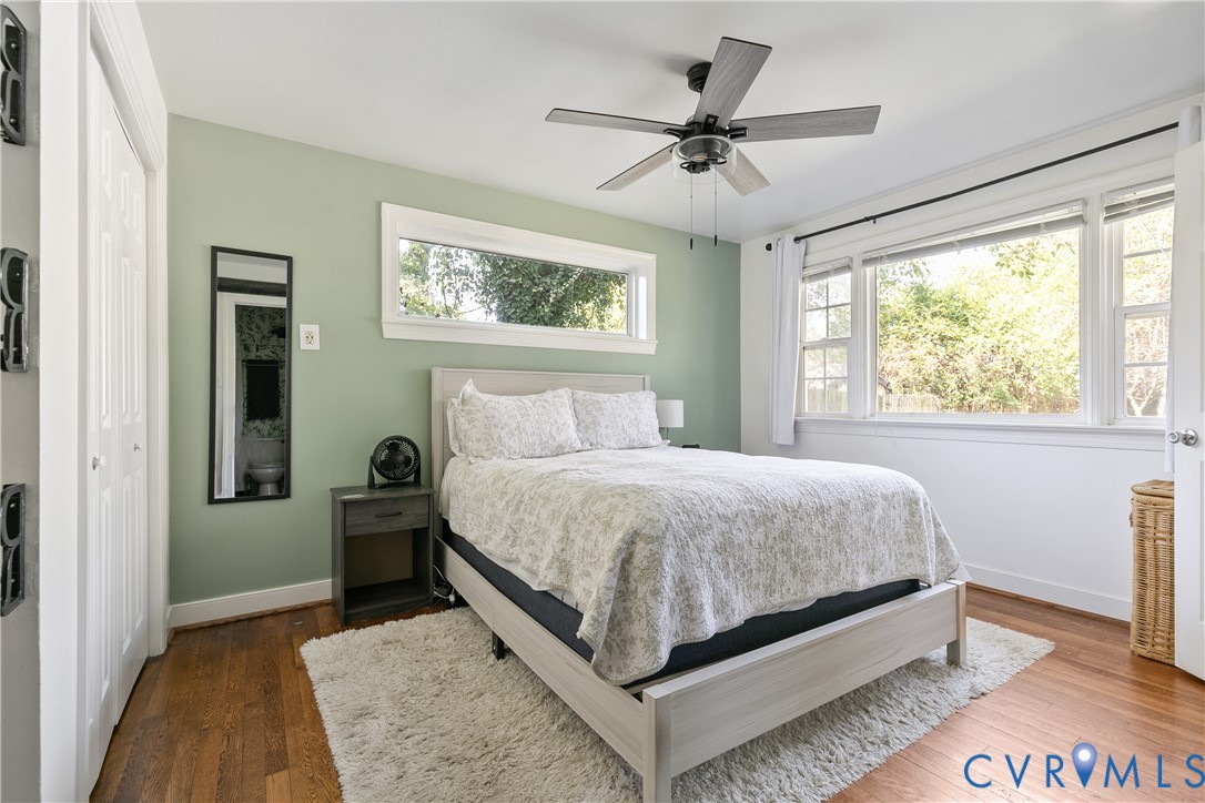 Wood-finish flooring, ceiling fan with integrated lighting, expansive multi-pane windows, and high-contrast dual-panel closet doors
