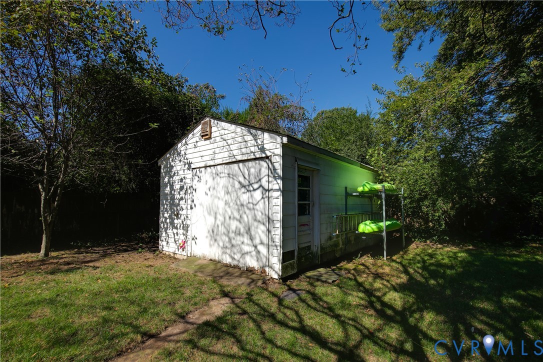 Detached single-car garage featuring white siding, a metal overhead door, and a side-entry pedestrian door, situated on a grass-covered lot with mature trees