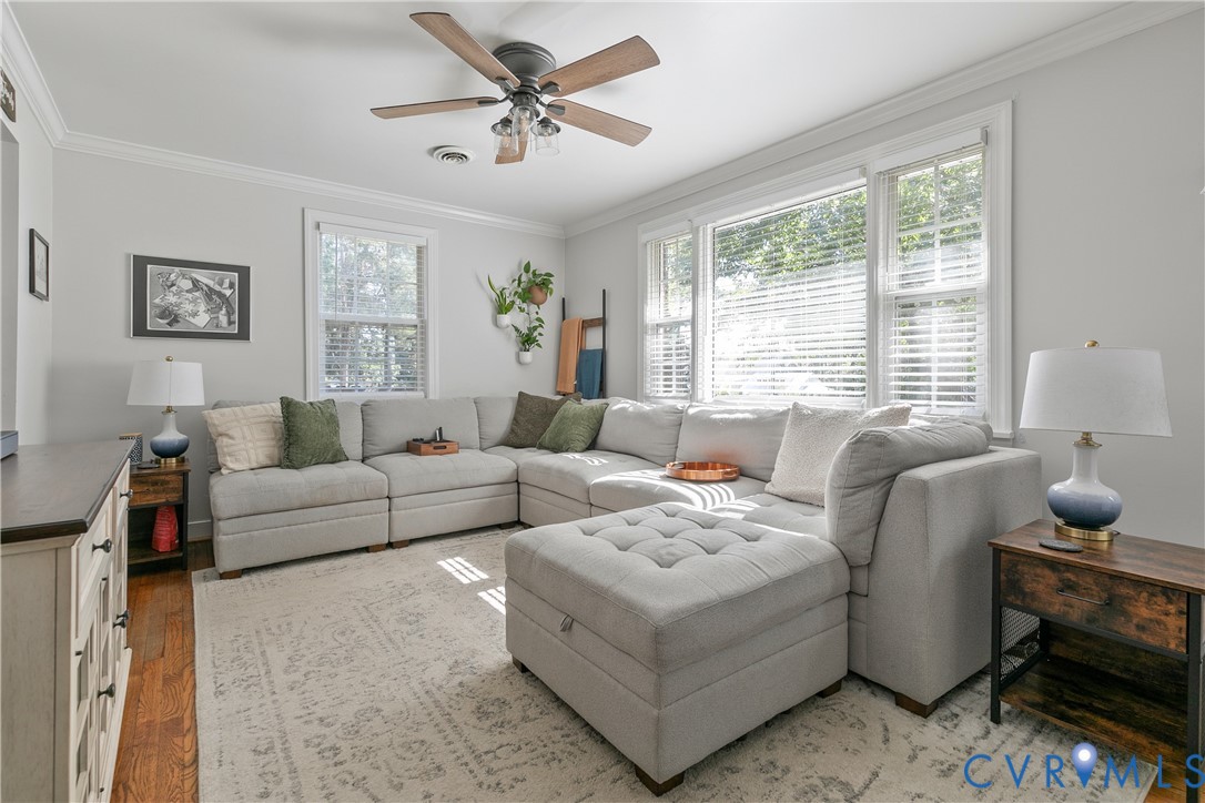 Living space featuring wood-finish flooring, multi-pane windows with white casing, and a ceiling fan with integrated lighting
