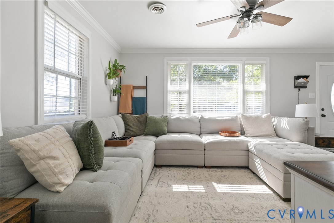 Living area featuring neutral wall paint, crown molding, multi-pane windows with horizontal blinds, and a ceiling fan with integrated lighting