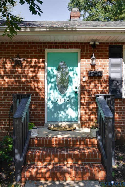Red brick exterior featuring a multi-pane glass insert front door, brick entryway steps, dark-tone handrails, and a chimney