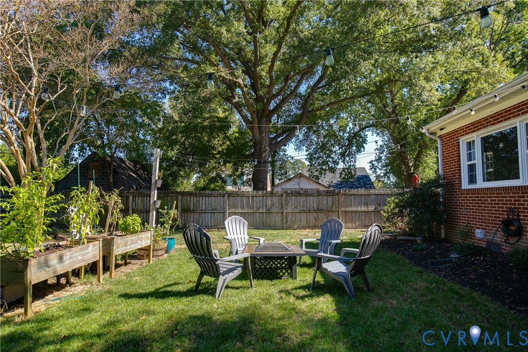 Backyard space featuring a brick exterior facade, raised wooden garden beds, wood privacy fencing, and overhead string lighting