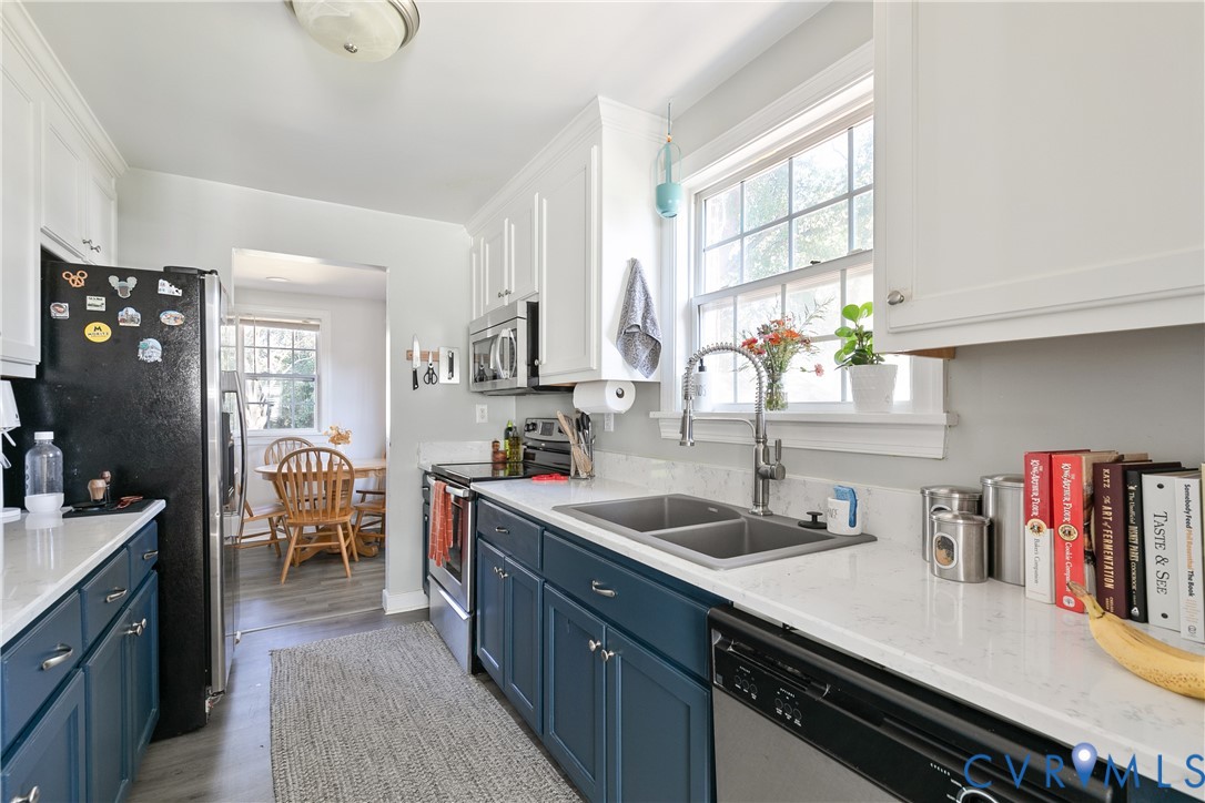Kitchen featuring two-tone shaker-style cabinetry, solid-surface countertops, dual-basin under-mount stainless steel sink with high-arch faucet, and stainless steel appliances