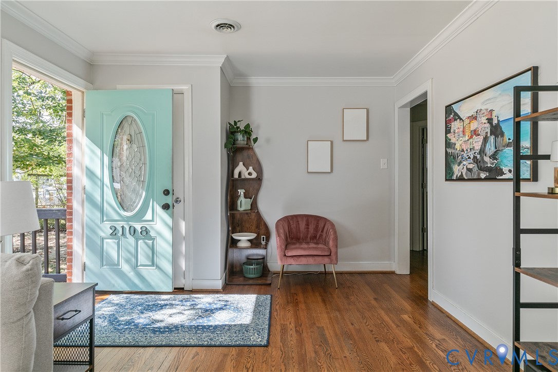 Entryway featuring wood-finish flooring, crown molding, and an exterior door with a decorative oval glass insert
