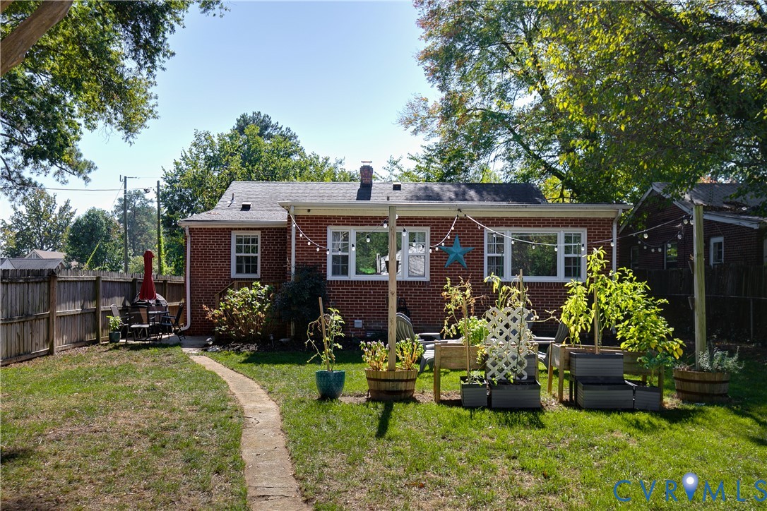 Brick exterior featuring a multi-pane window configuration, a stone pathway, a wood privacy fence, and raised planter boxes