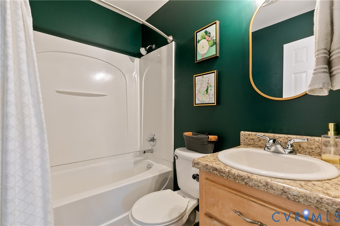 Bathroom featuring a white molded tub-and-shower surround, stone-composite countertop, light-wood cabinetry, and arched wall mirror with a metallic frame