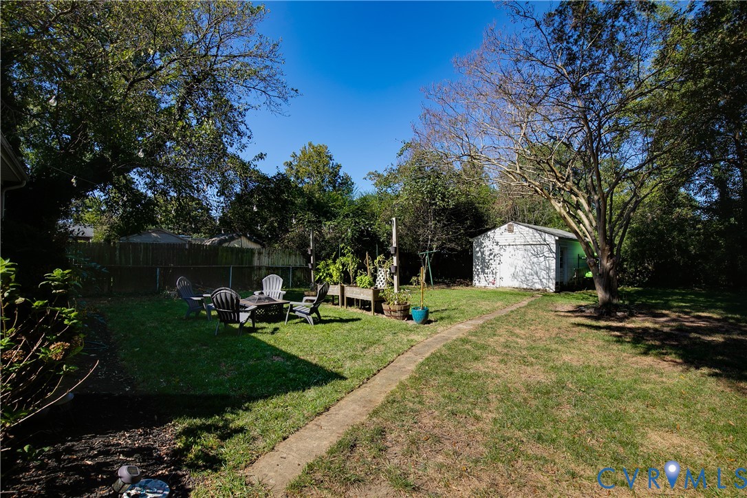 Expansive backyard featuring a mature canopy of trees, a detached storage structure, a stone-surfaced path, and a wooden privacy fence
