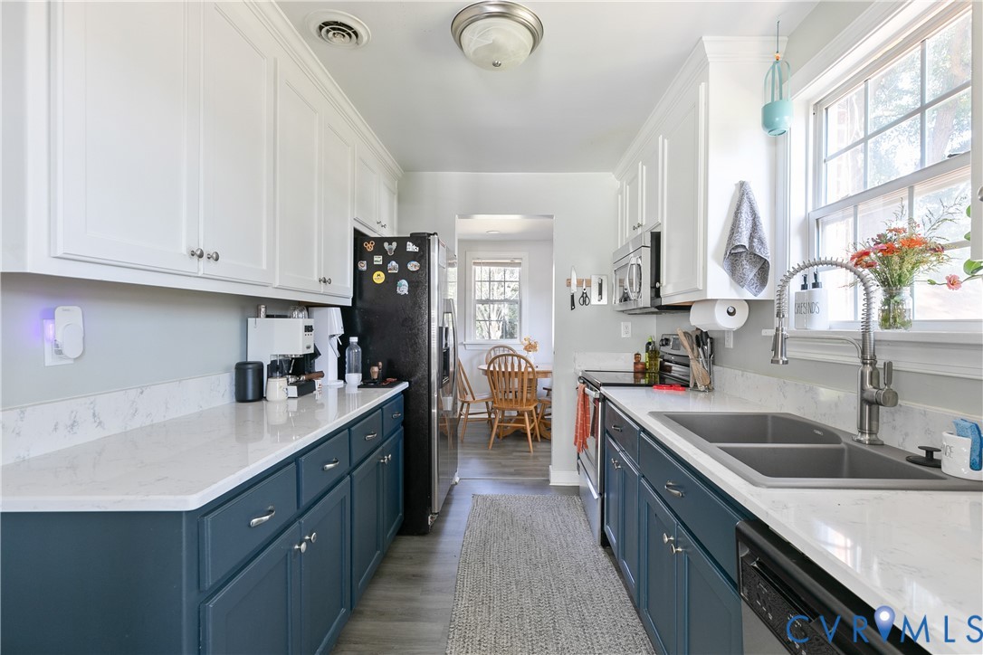 Galley kitchen featuring dual-tone cabinetry, quartz countertops, dual-basin undermount sink with arched pull-down faucet, and wood-finish flooring