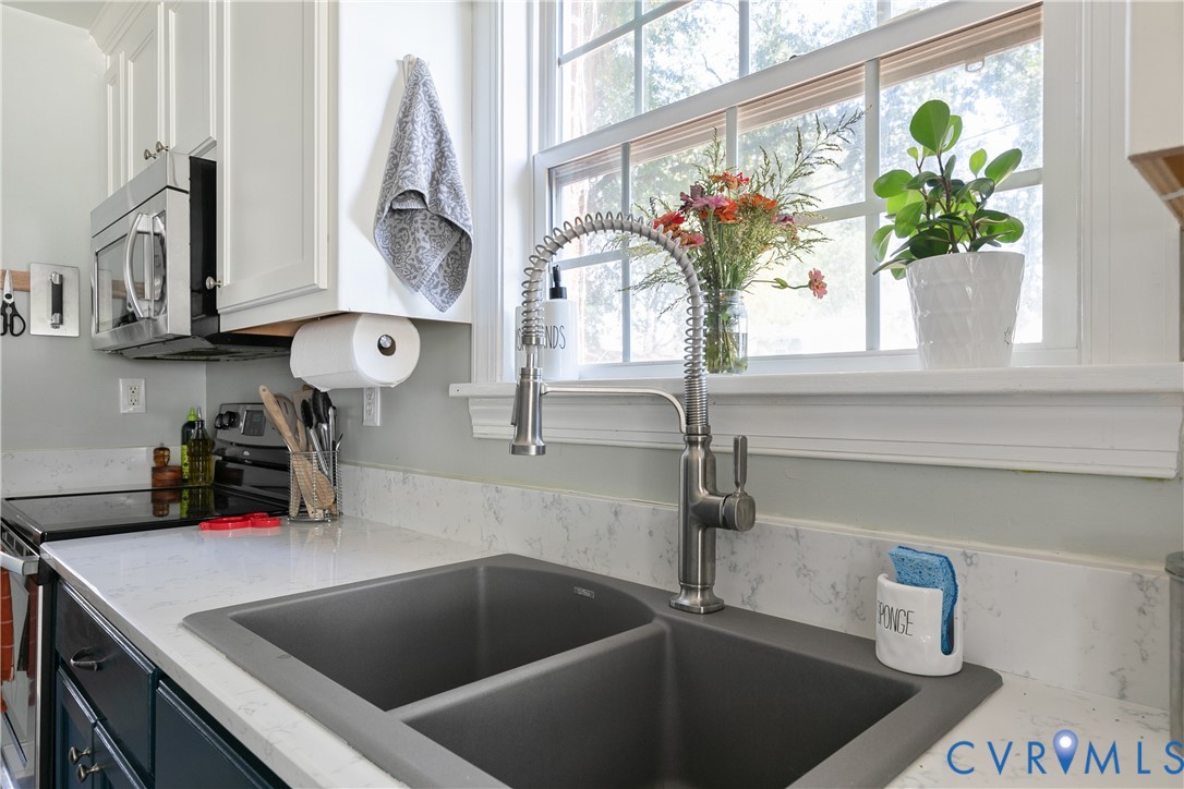Kitchen featuring stone-finish countertops, undermount double-basin sink, high-arc pull-down faucet, white cabinetry, and stainless steel over-the-range microwave