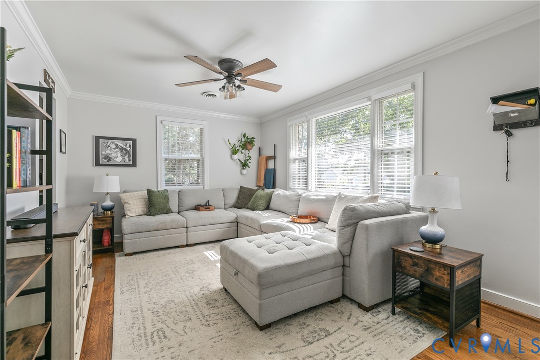 Hardwood flooring, crown molding, ceiling fan with light fixture, and multiple windows with horizontal blinds