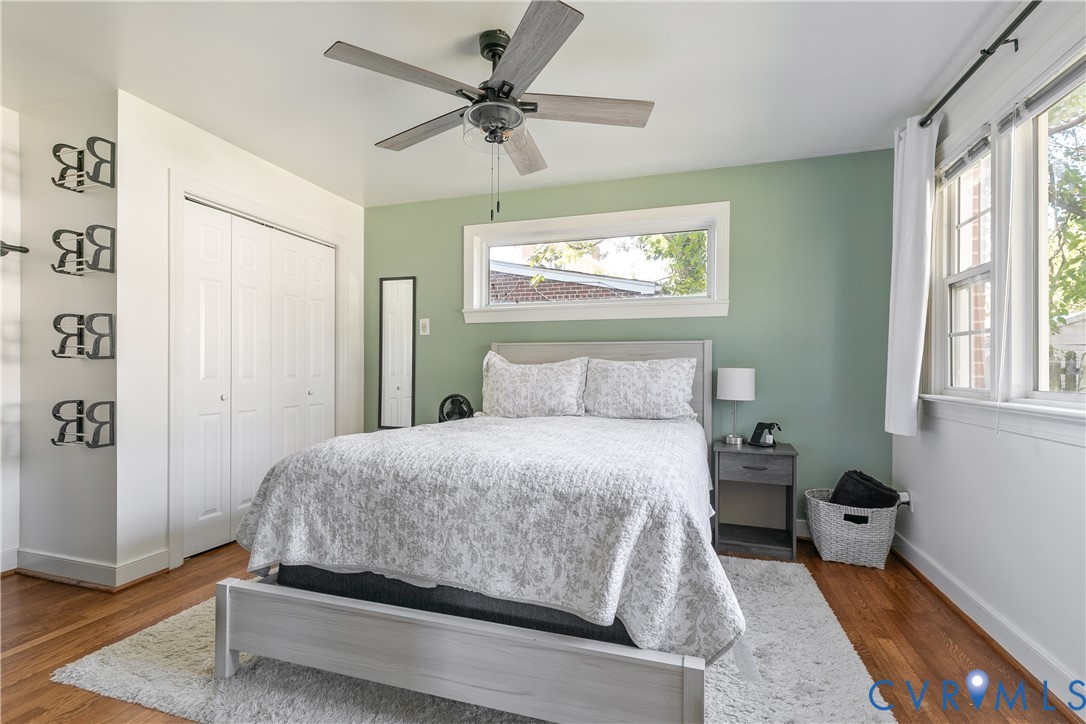 Bedroom featuring hardwood flooring, multi-panel bi-fold closet doors, ceiling fan with light fixture, and horizontal window