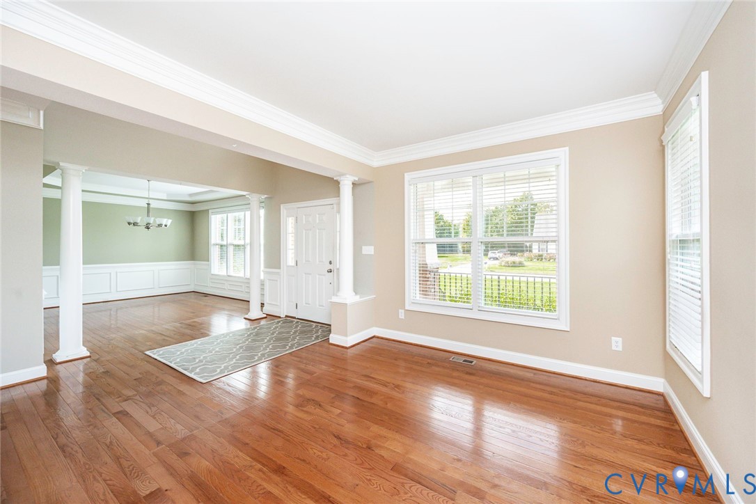 Open interior featuring wood-finish flooring, crown molding, white classical-style support columns, and wainscoting