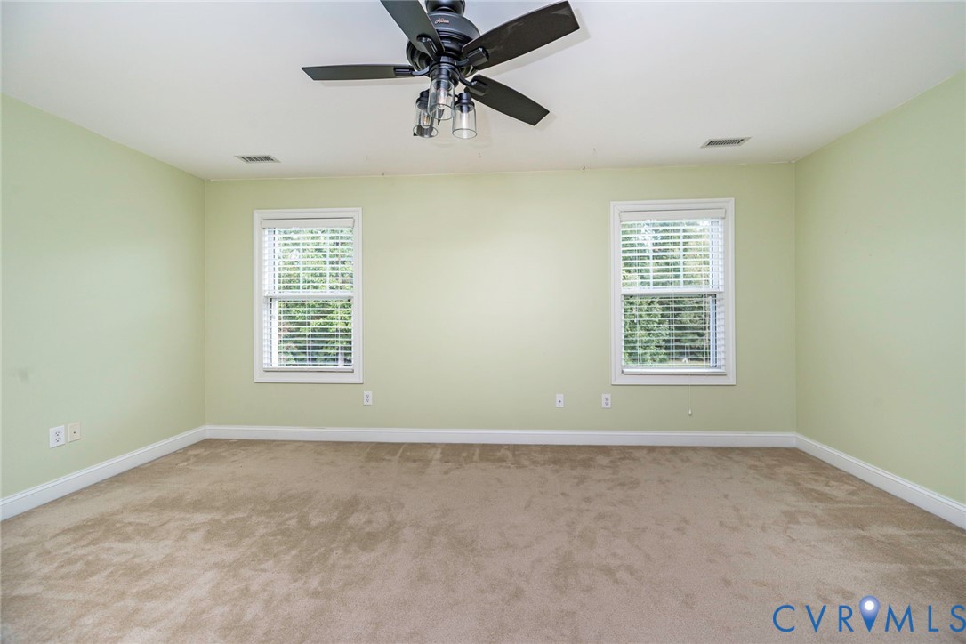 Neutral-toned carpeted flooring, two double-hung windows with horizontal blinds, and a multi-blade ceiling fan with integrated lighting