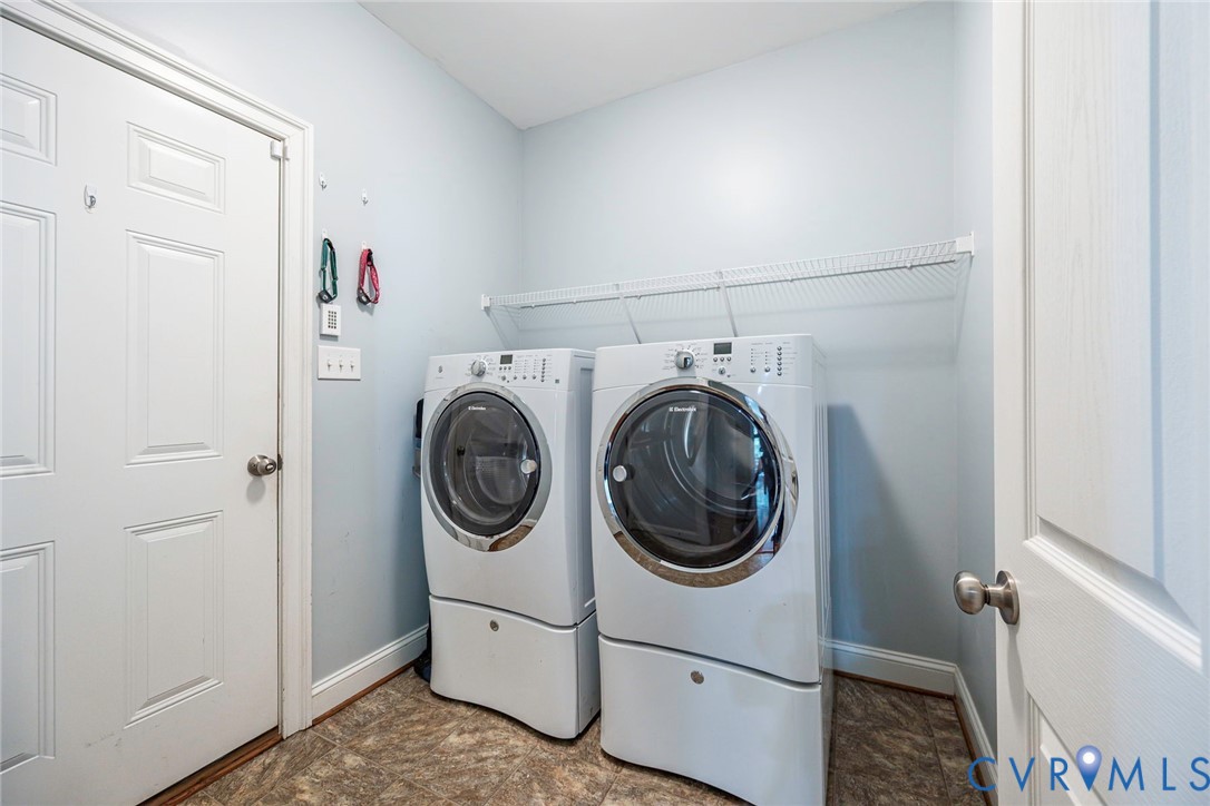 Utility room featuring white front-loading appliances, patterned vinyl flooring, and wall-mounted wire shelving
