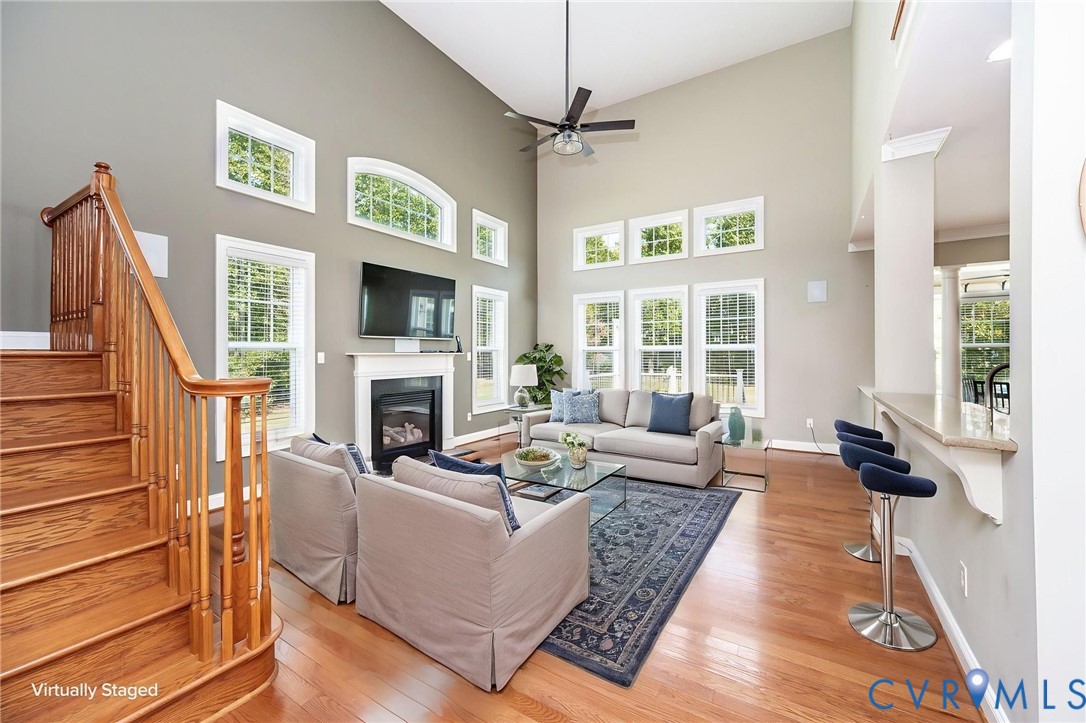 Vaulted ceilings, fireplace with mantel, wood-finish flooring, staircase with wooden balustrade, and breakfast bar