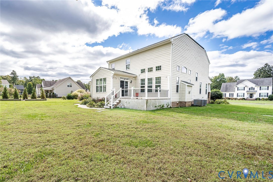 Two-story residence featuring light-colored horizontal siding, a raised rear deck with balustrades, multiple windows, and a large level lawn