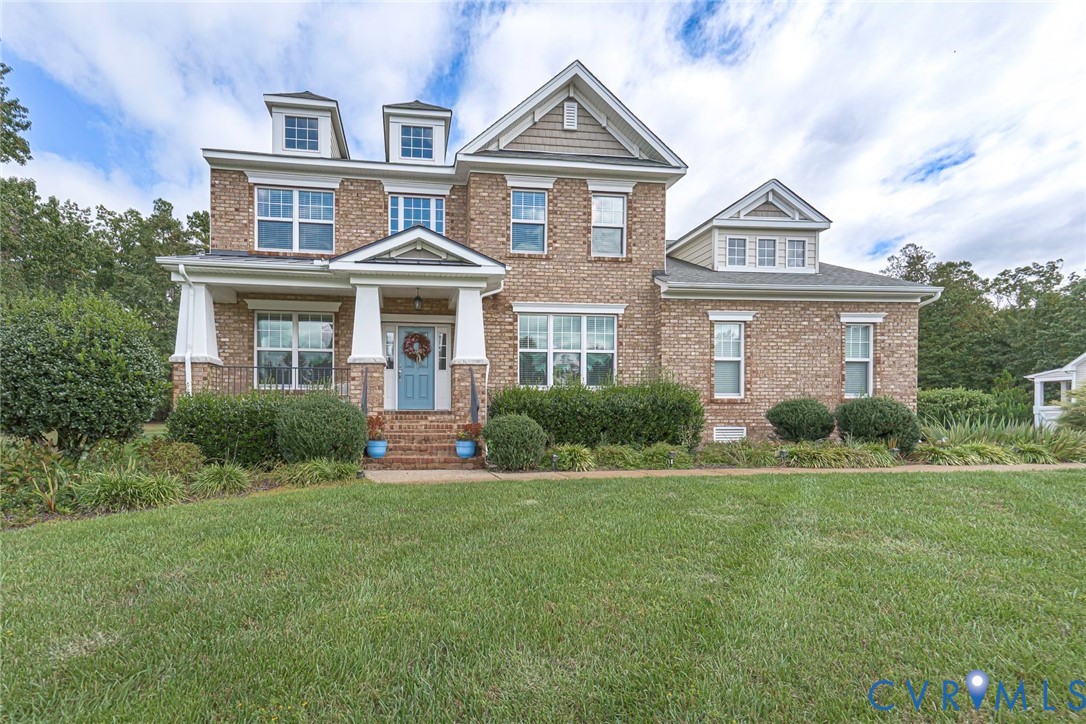 Multi-story brick exterior featuring a covered front porch with white columns, dual dormer windows, multi-pane windows, and a shingle roof Multi-story brick exterior featuring a covered front porch with white columns, dual dormer windows, multi-pane windows, and a shingle roof