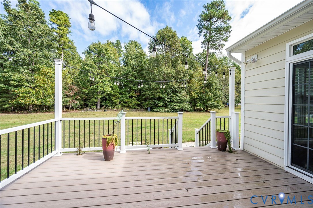 Elevated rear deck featuring composite decking, white posts, and black metal balusters with integrated overhead string lighting
