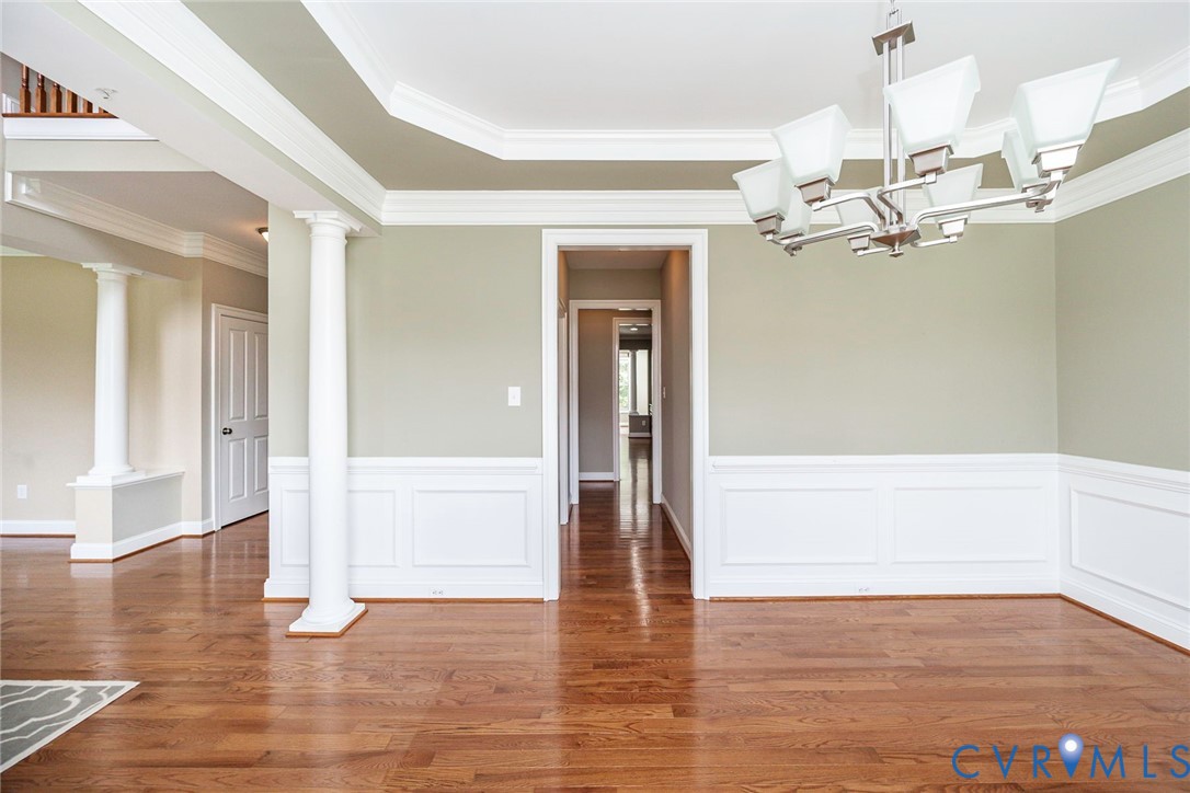 Hardwood flooring, crown molding, chair rail wainscoting, decorative columns, and a multi-arm chandelier