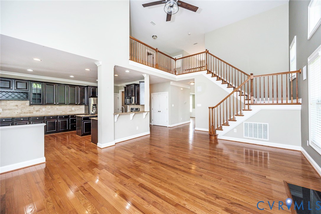 Open-concept interior featuring vaulted ceilings, wood-finish flooring, dark-toned built-in cabinetry, and a staircase with a wooden balustrade