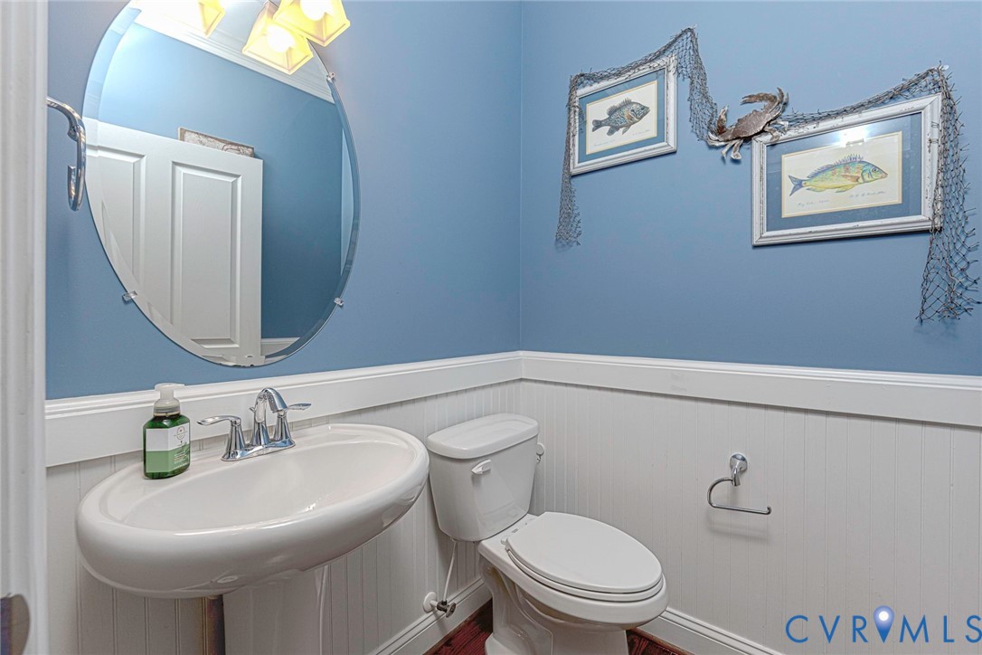 Oval frameless mirror, white pedestal sink with chrome dual-handle faucet, wainscoting, and polished metal hardware