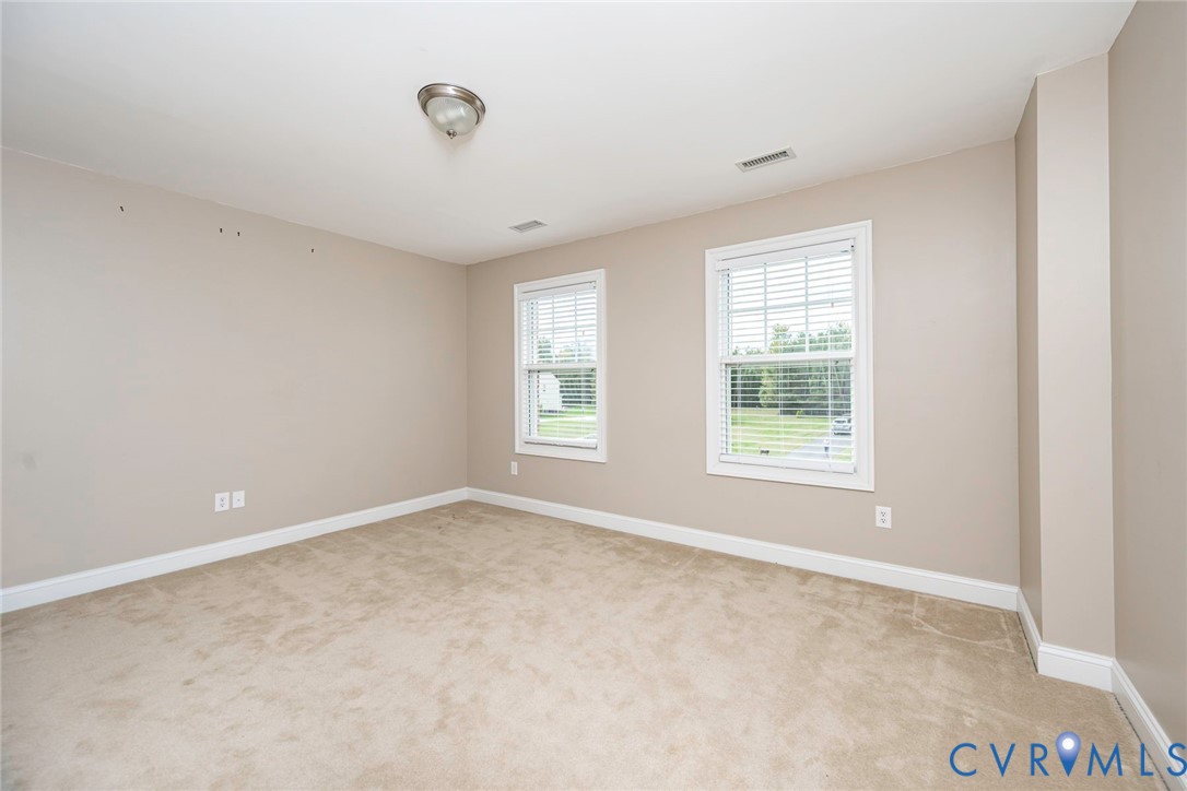 Neutral-toned room featuring wall-to-wall carpeting, dual windows with integrated blinds, and a flush-mount ceiling fixture