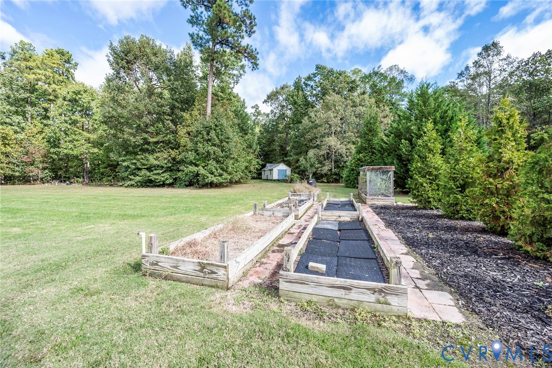 Backyard featuring wood-frame raised garden beds, manicured lawn, established perimeter trees, and a detached storage structure