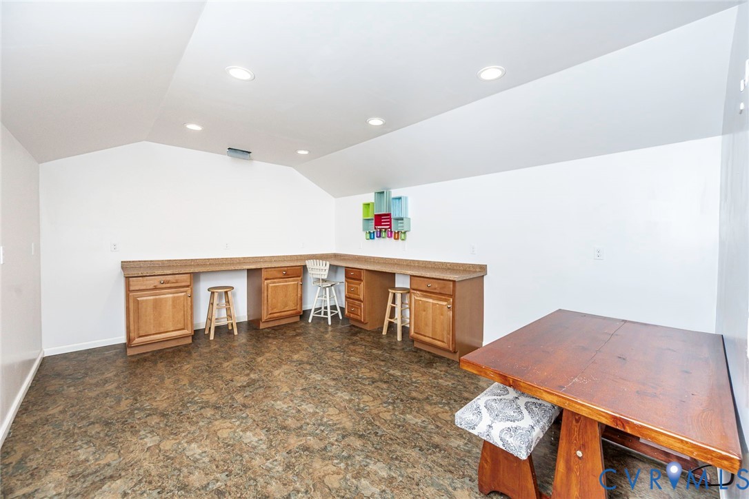 Built-in wooden cabinetry featuring stone-finish countertops, recessed ceiling lighting, and hard-surface flooring under a vaulted ceiling