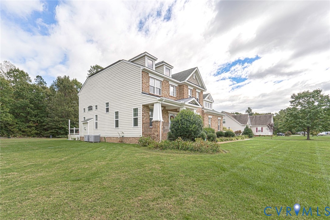 Multi-story residence featuring brick and siding exterior, front-facing dormer windows, covered porch with tapered columns, and expansive lawn