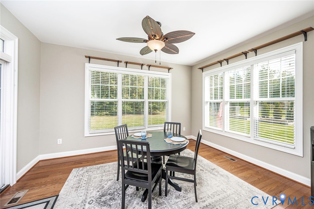 Wood-finish flooring, ceiling fan with integrated light fixture, and multiple large windows featuring horizontal blinds and decorative wall-mounted shelving brackets