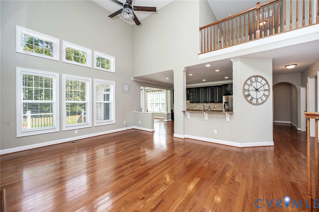 Vaulted ceilings featuring a ceiling fan, wood-finish flooring, two-story windows, and a mezzanine with a wooden railing overlooking the main floor