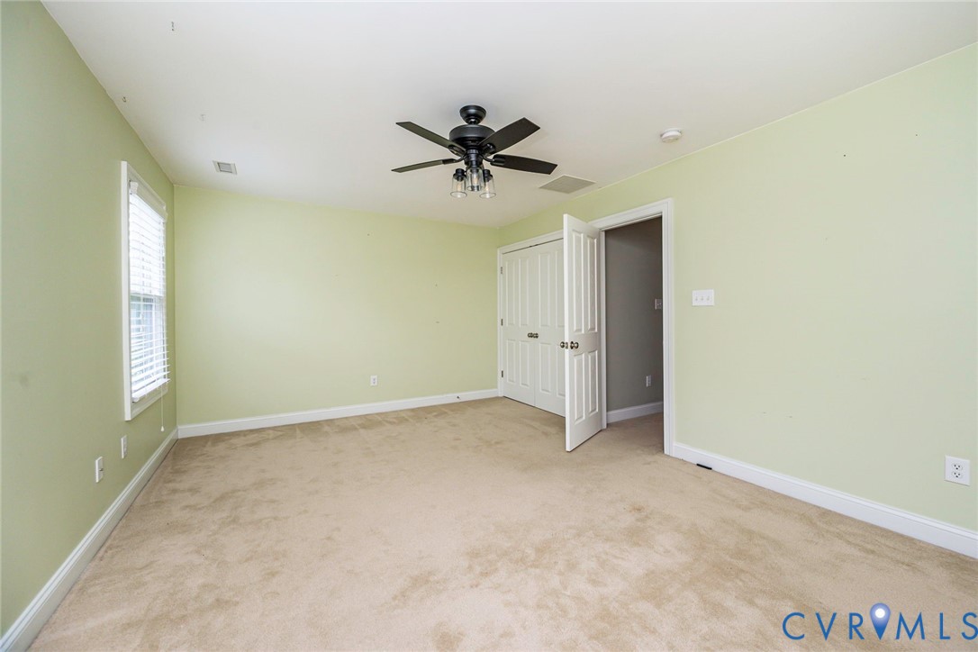 Room featuring neutral carpeting, double-door closet, multi-blade ceiling fan with integrated lighting, and window with blinds