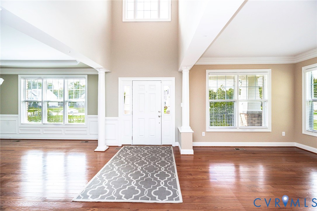 Entryway featuring high ceilings, wood-finish flooring, white architectural columns, expansive windows, and crisp crown molding