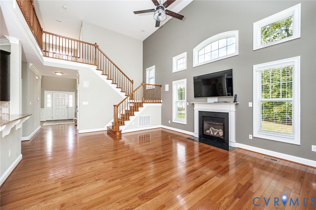 Vaulted ceilings, wood-finish flooring, fireplace with a mantle, wood-railing staircase, and tiered windows