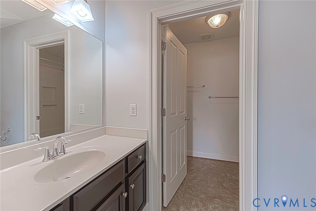 Vanity featuring a solid-surface countertop with an integrated oval sink and dark-toned cabinetry, complemented by a large wall-mounted mirror, brushed-finish fixtures, and a six-panel door opening to a storage area with tile flooring and installed hardware