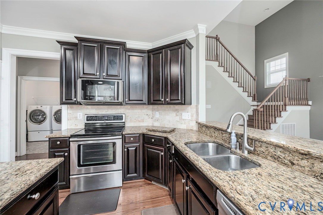 Kitchen featuring dark-finish cabinetry, stone countertops, stainless steel appliances, a tile backsplash, and wood-finish flooring