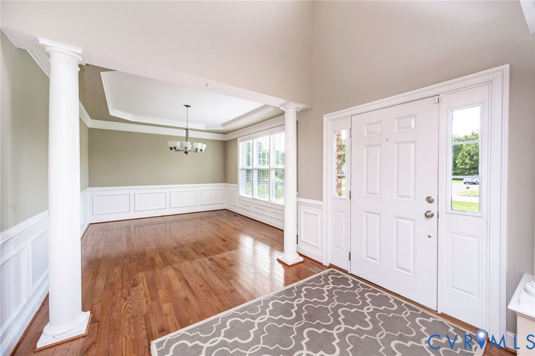 Foyer featuring vaulted ceilings, wood-finish flooring, decorative columns, wainscoting, and a multi-light chandelier