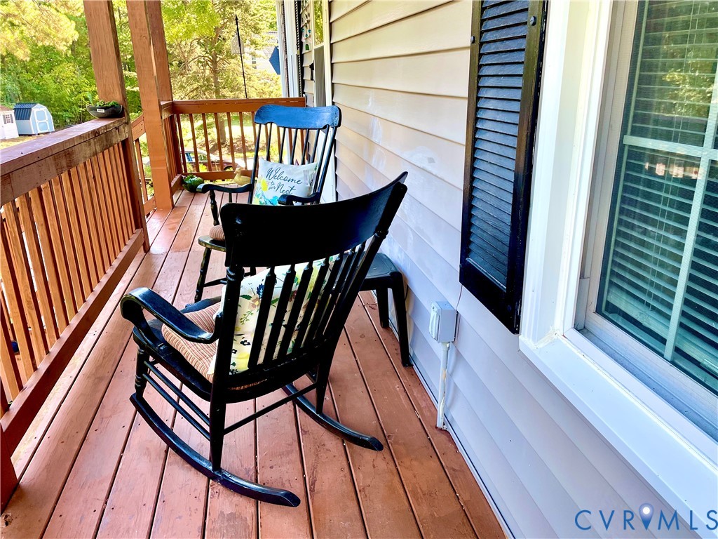 Covered porch featuring wood-finish decking, natural wood railings, horizontal siding, and decorative window shutters