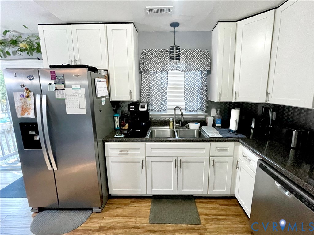 Kitchen featuring white shaker-style cabinetry, dark stone-finish countertops, stainless steel appliances, a double-basin stainless steel sink, and wood-finish flooring