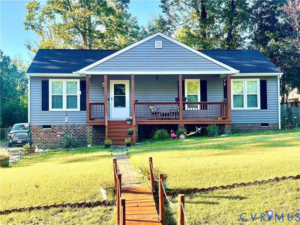 Ranch-style exterior featuring grey siding, a front porch with wood railing, brick foundation detailing, and a multi-paneled front door