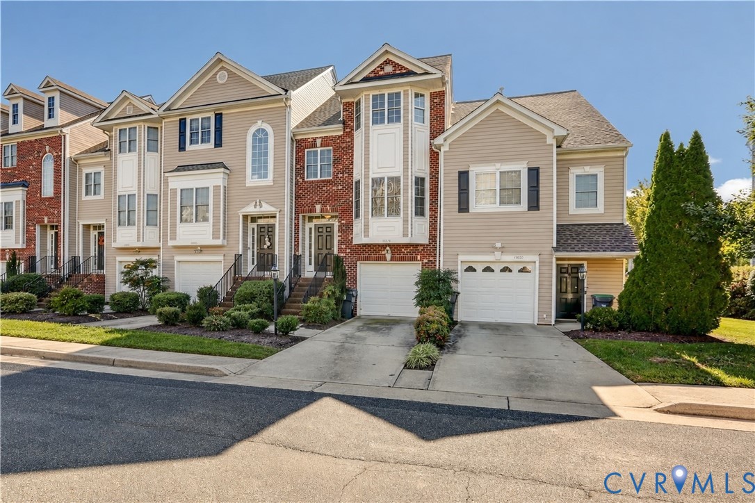 Multi-story townhome exterior featuring horizontal lap siding and brick veneer, gabled rooflines, attached garage with arched-top windows, and arched window accents