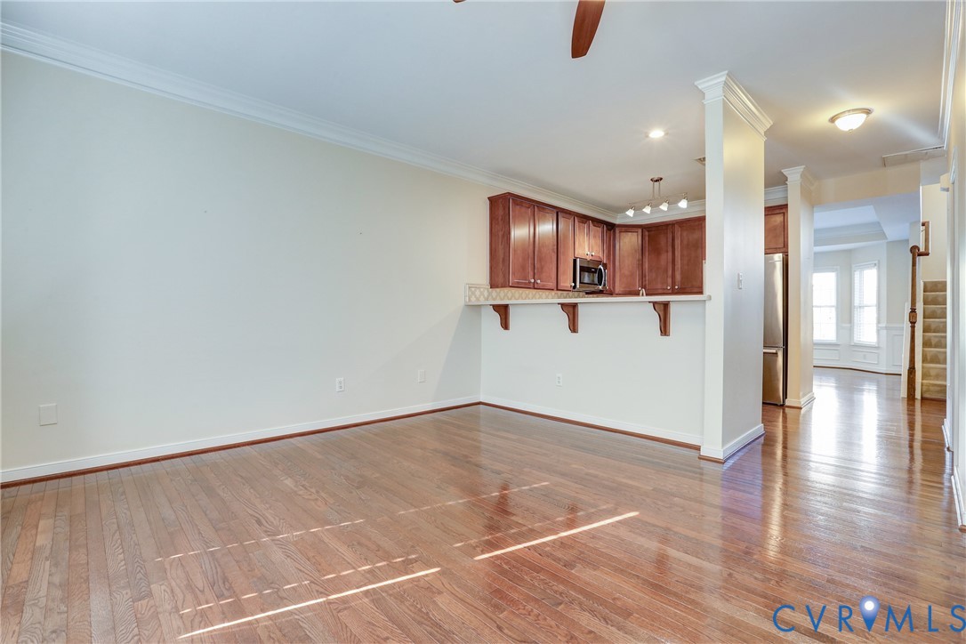 Open floor plan featuring wood-finish flooring, crown molding, kitchen with dark-finish cabinetry, breakfast bar, and stainless steel appliances
