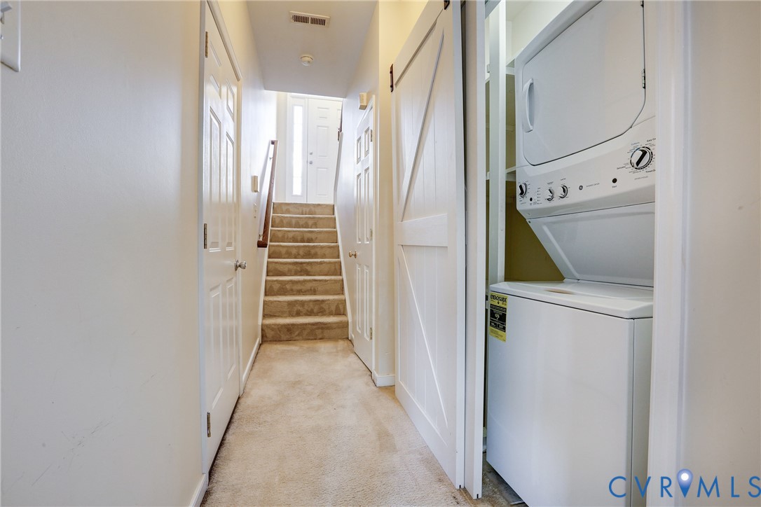Laundry area featuring a stackable washer and dryer unit, white interior doors, a white barn-style sliding door, and carpeted flooring