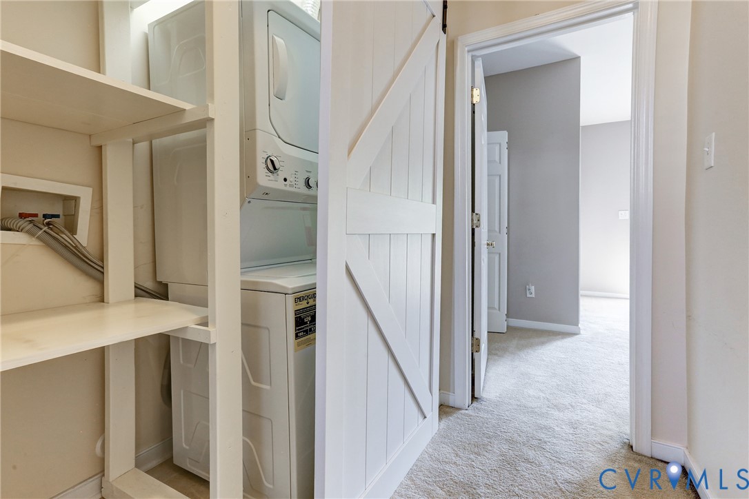 Laundry closet featuring a white sliding barn-style door, stacked laundry unit, and built-in shelving