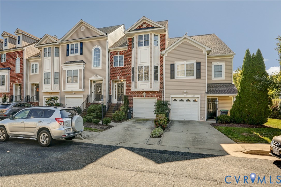 Multi-story townhouse exterior featuring a brick and vinyl siding facade, arched window detailing, gabled rooflines, and attached garage entries