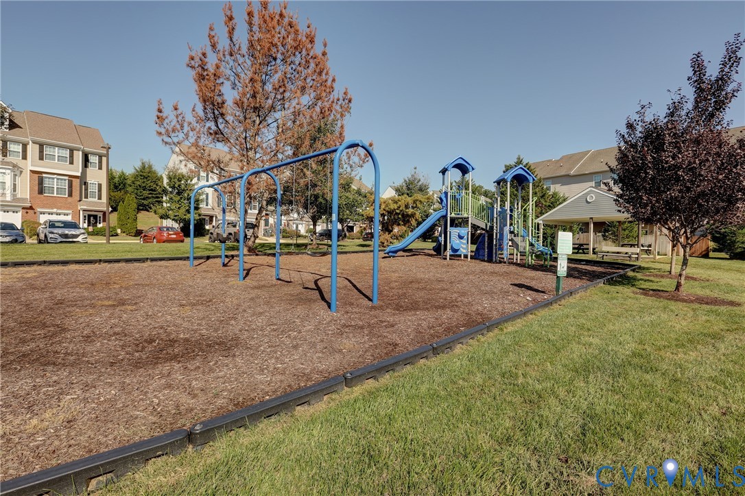 Community recreational area featuring a playground with a swing set and slide, wood mulch surfacing, and an attached covered pavilion