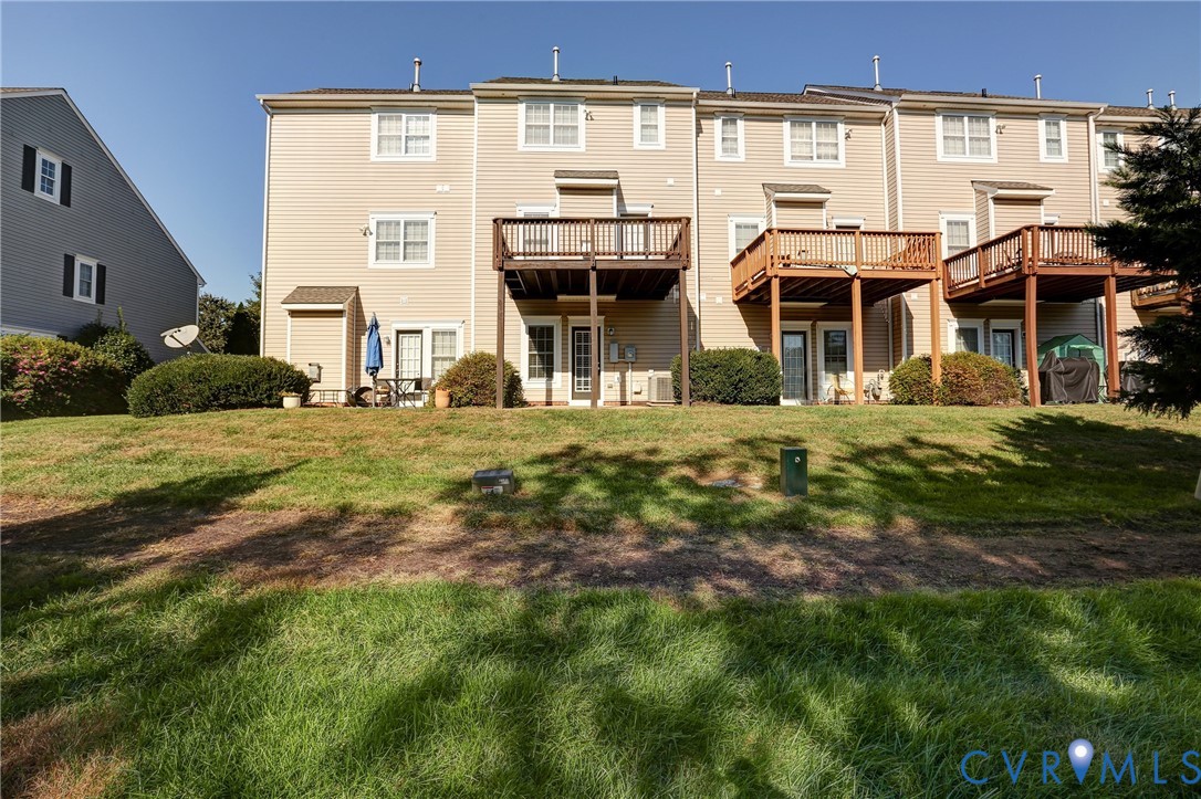 Multi-level townhouse exterior featuring horizontal siding, elevated wooden decks, and grass lawn grounds