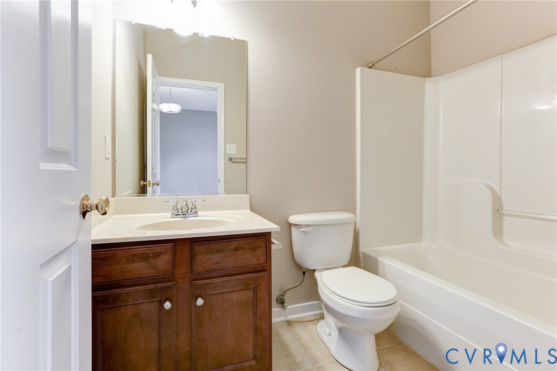 Bathroom featuring a dark wood-finish vanity, solid-surface countertop, rectangular wall-mounted mirror, and a tub-shower combination with an integrated surround