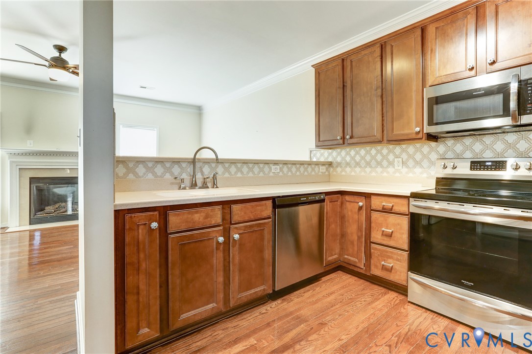 Kitchen featuring wood cabinetry, stainless steel appliances, patterned tile backsplash, and wood-finish flooring