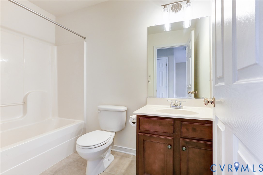 Bathroom featuring a vanity with dark-finish wood cabinetry, a light-toned countertop, an integrated oval basin, a wall-mounted mirror, and a tub-shower combination with a surround
